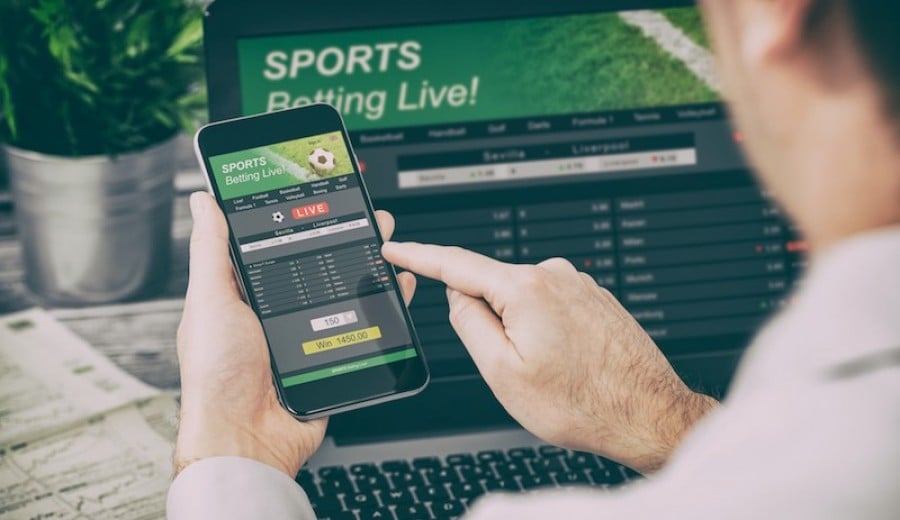 Man betting on sport on a phone with laptop open Man betting on sport on a phone with laptop open